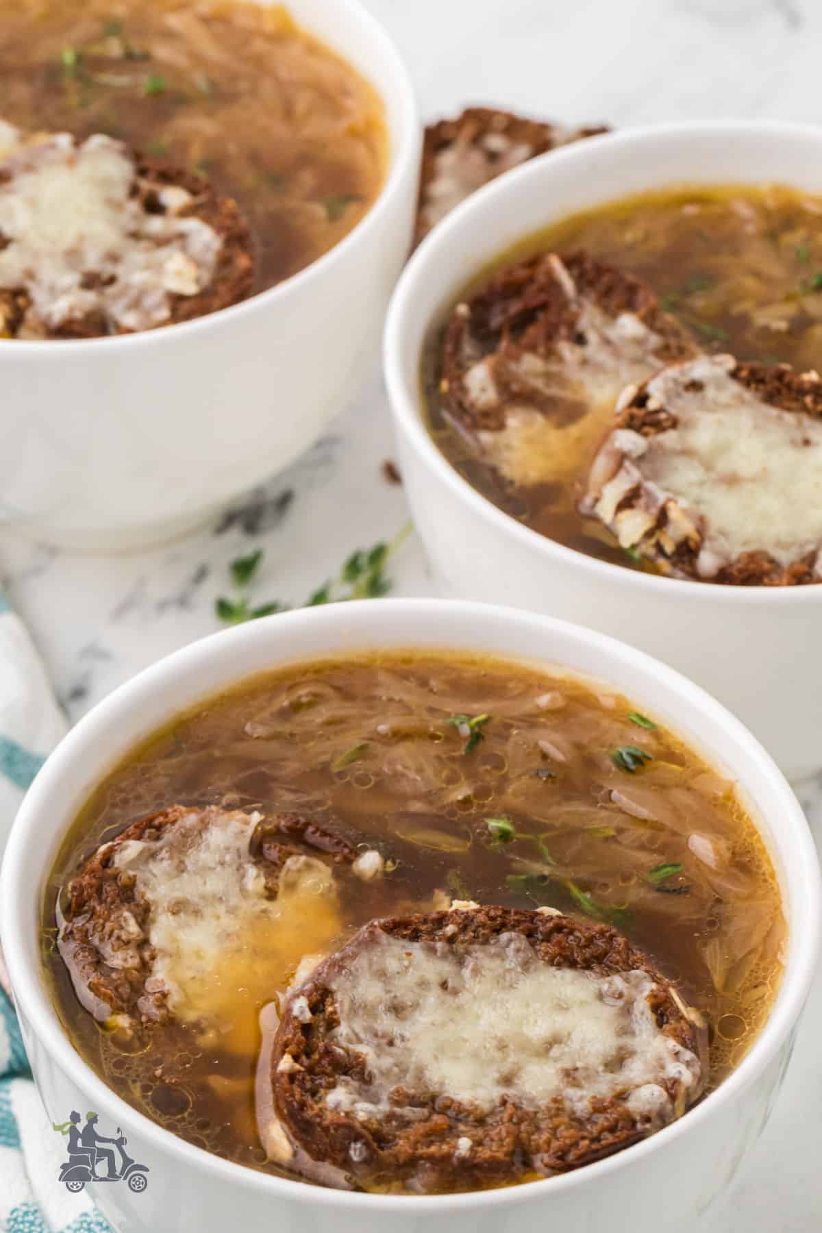 Slow cooker French Onion Soup served in white soup mugs and topped with toast and melted cheese. 