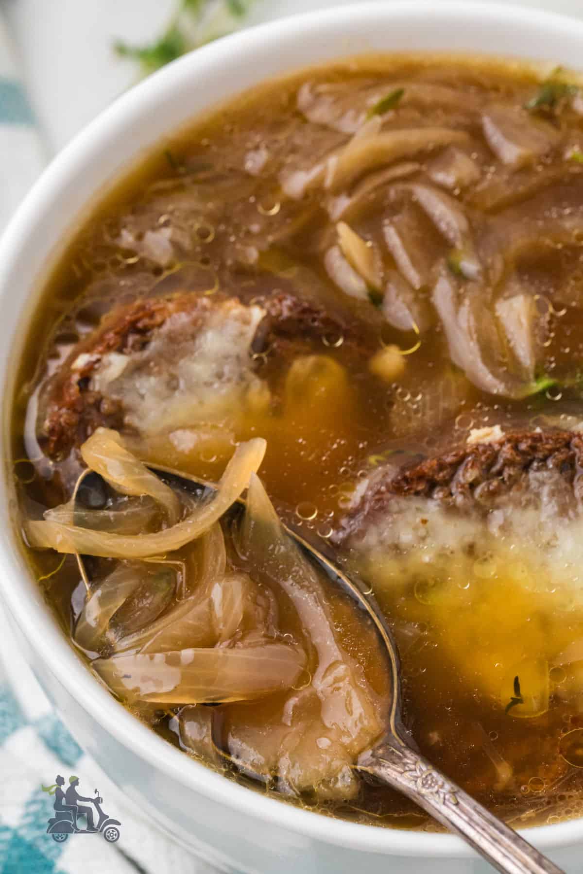 A closeup of a bowl of French Onion Soup with a spoon holding a sip. 