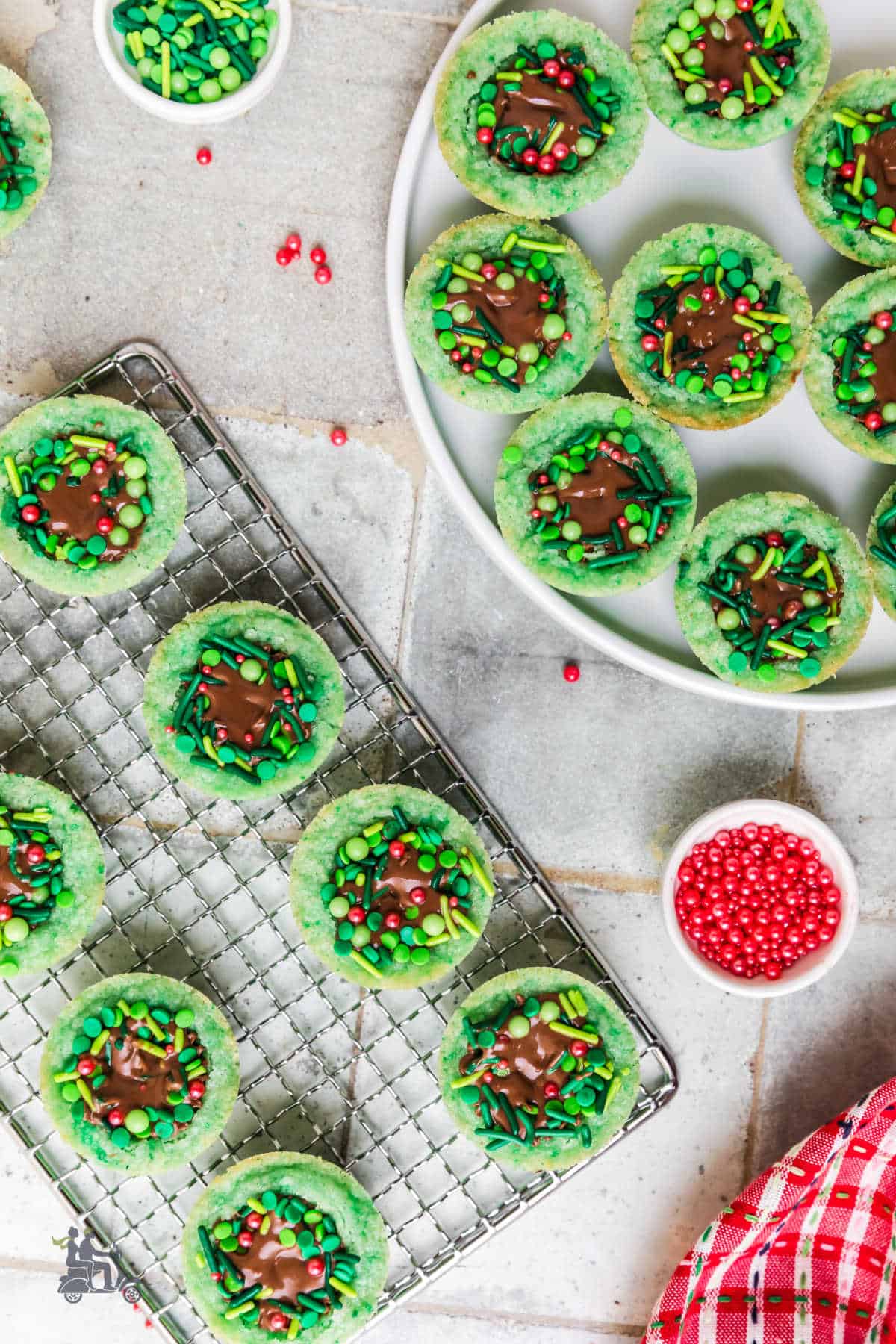 Sugar cookie wreaths decorated on a wire rack and on a white serving plate. 