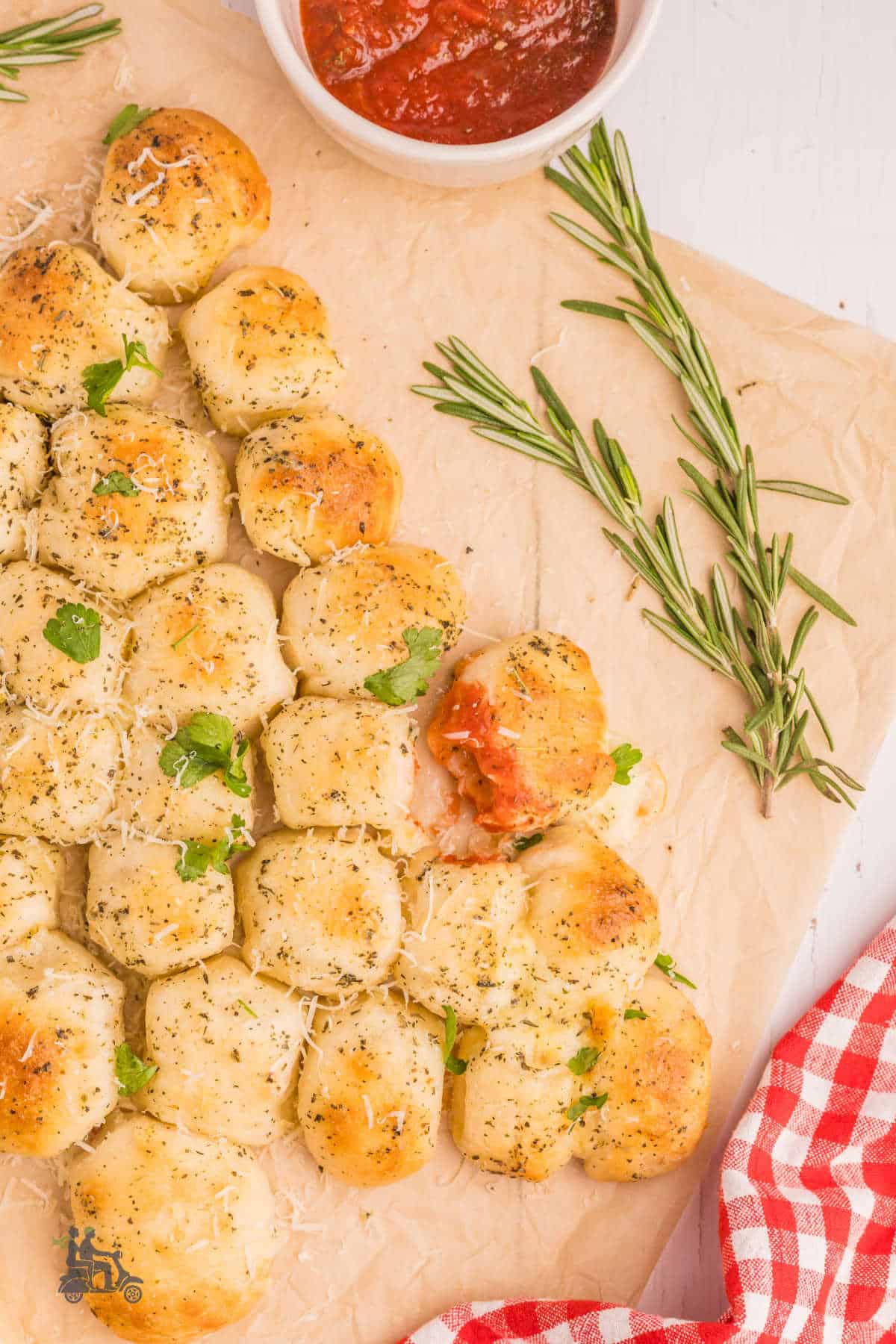 Festive pull-apart bread on a wooden cutting board with one roll dipped in Marinara Sauce.