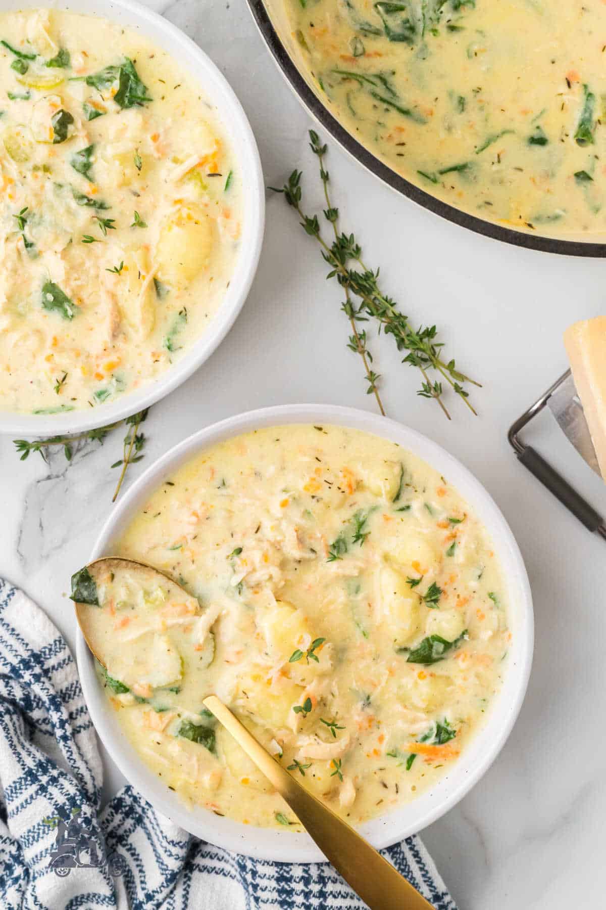 Easy chicken gnocchi soup with spinach in white bowls with a spoon in one bowl.