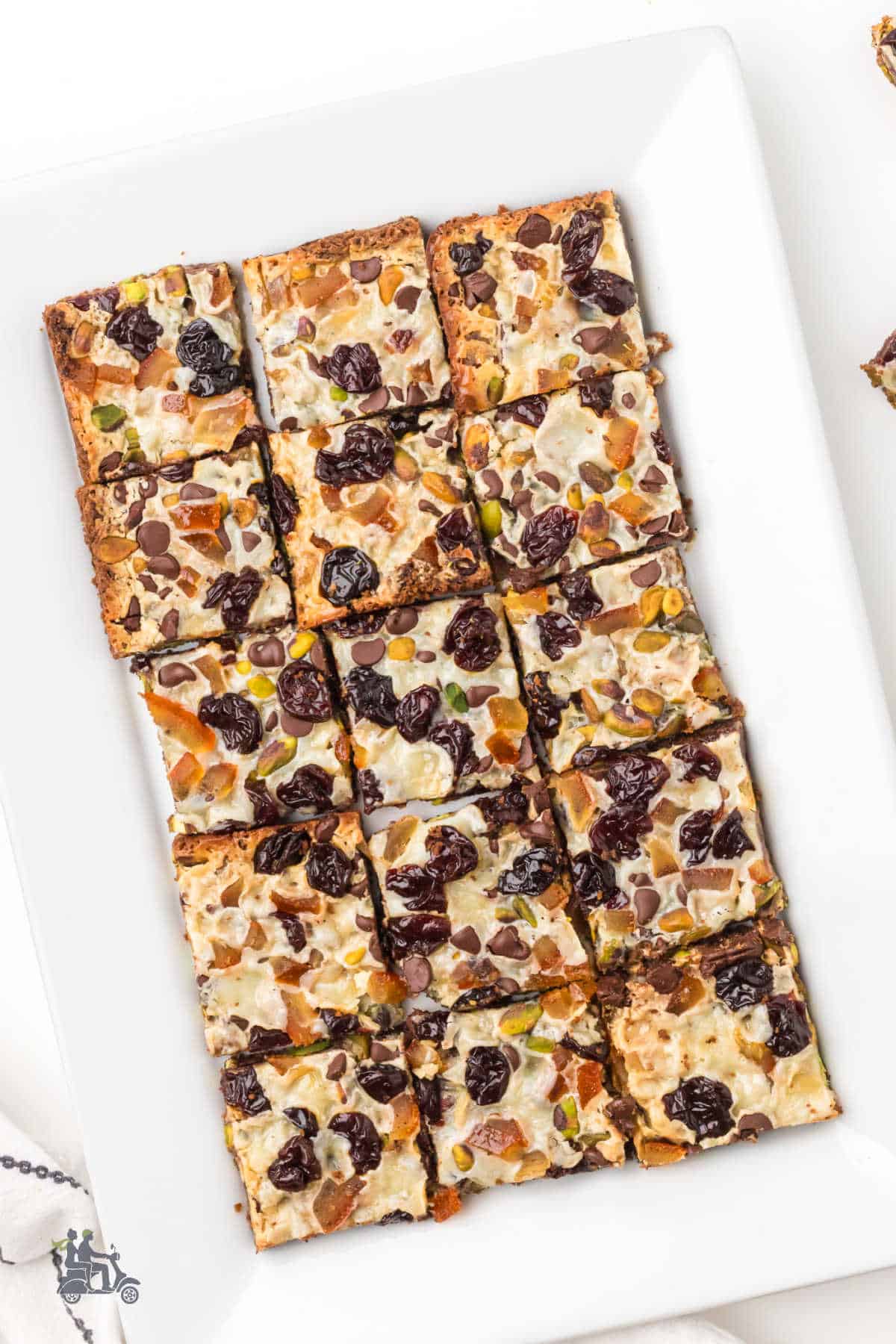 Plate of pistachio and cherry holiday magic bars dusted with orange peel. 