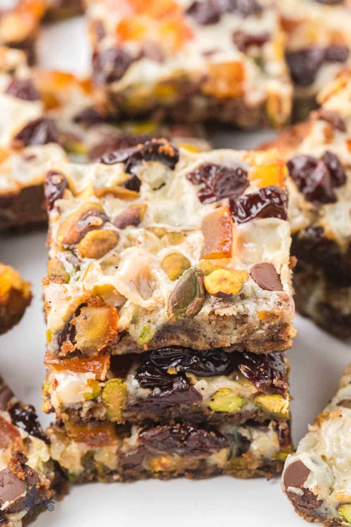 Closeup of holiday cookie bars with pistachios, chocolate chips, cherries, and condensed milk. 