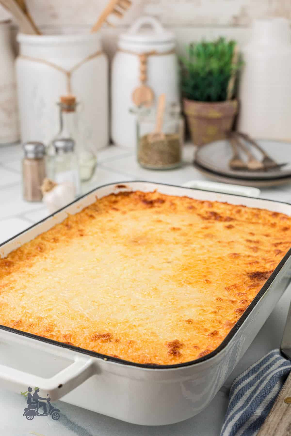 A beef moussaka casserole in a white baking dish, cooling on a wire rack. 