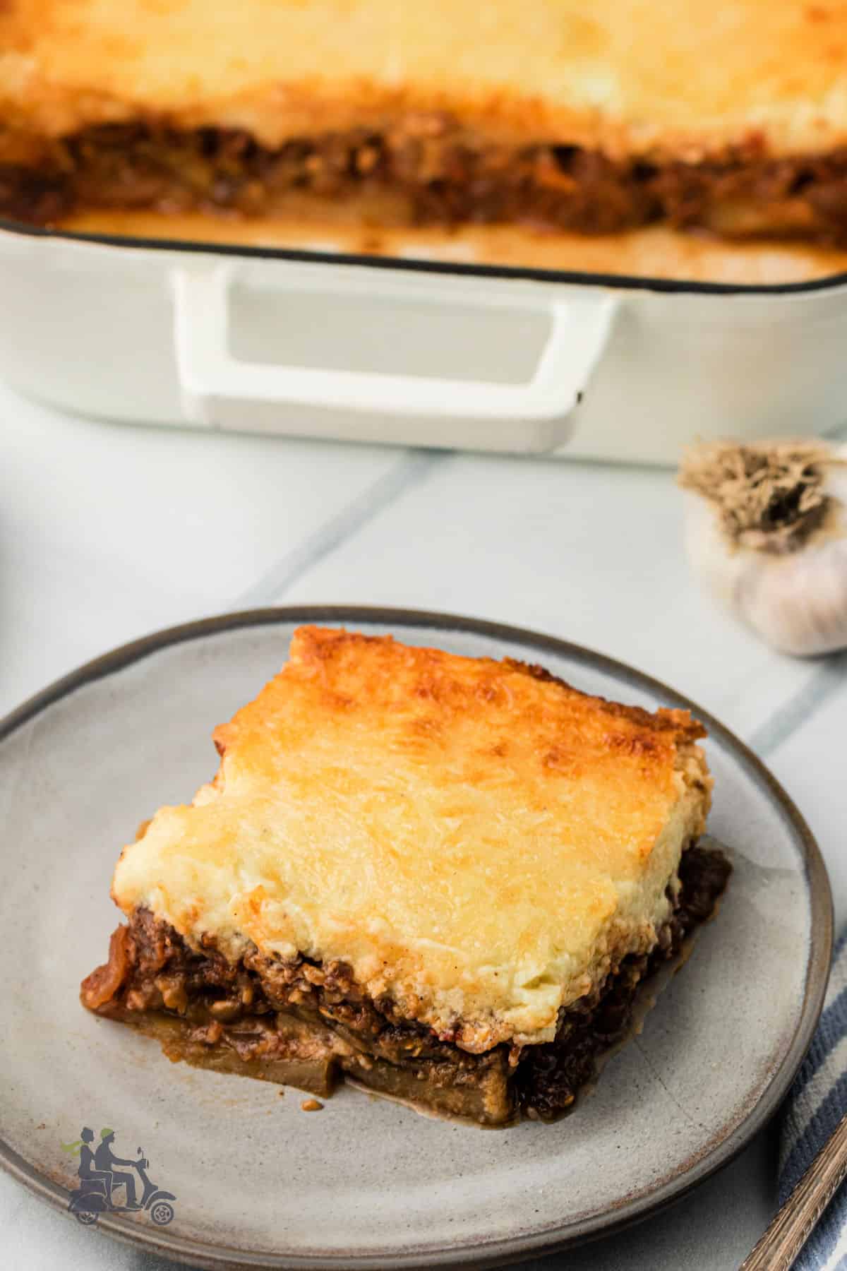 Layered eggplant and meat sauce baked in a casserole dish with a square set on a luncheon plate. 