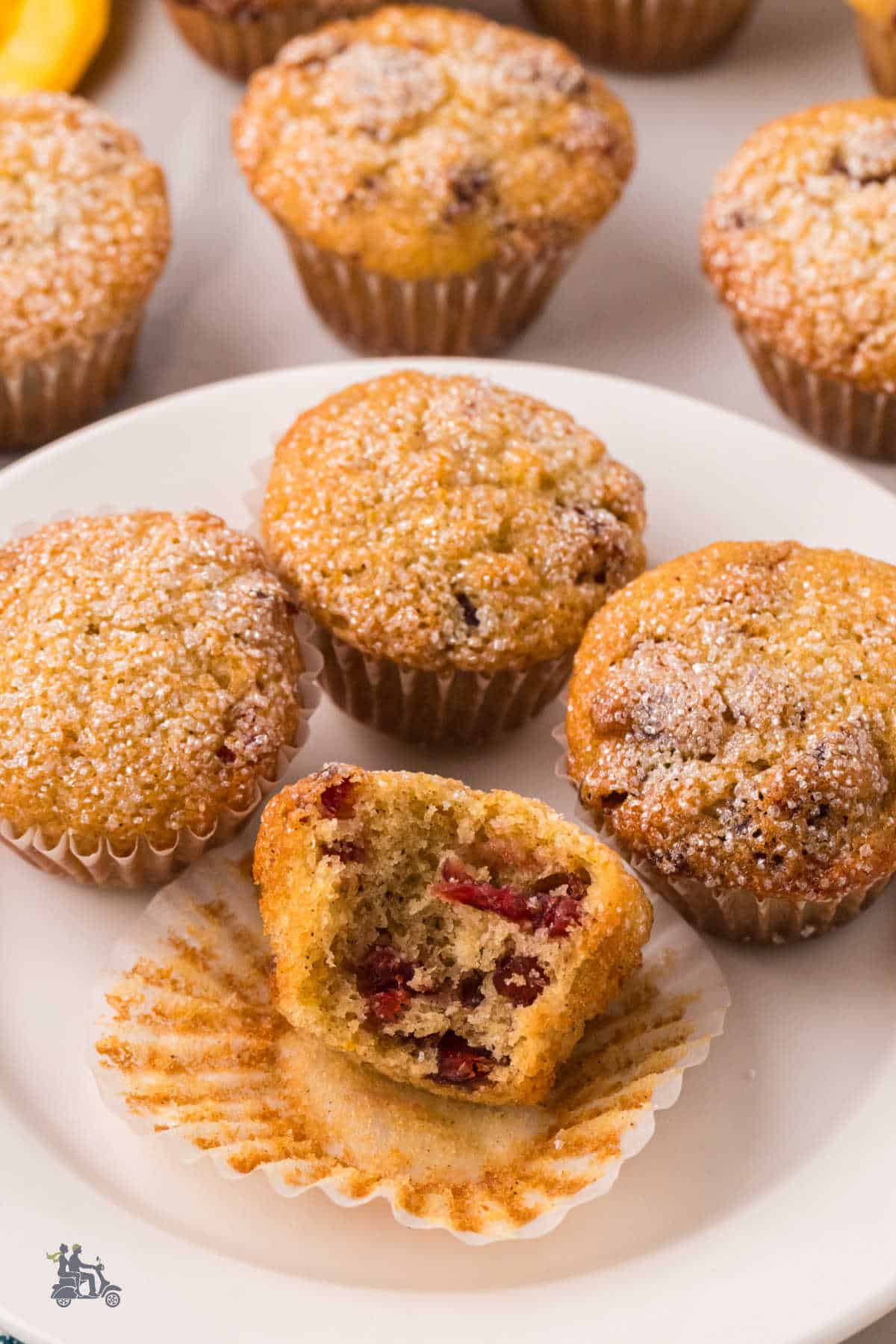 A white plate with Cranberry orange mini muffins and one split in half to show the fruit inside.