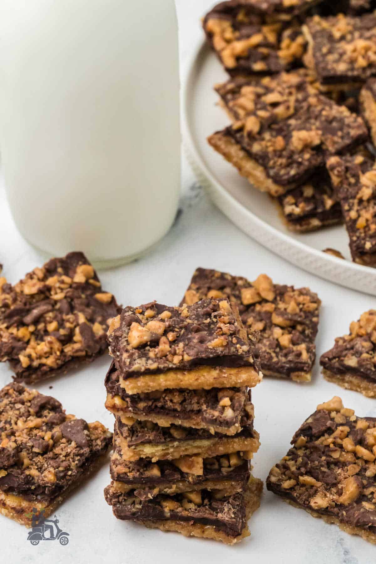 Chocolate toffee bark piled on a table and plate with a container of milk in the background.