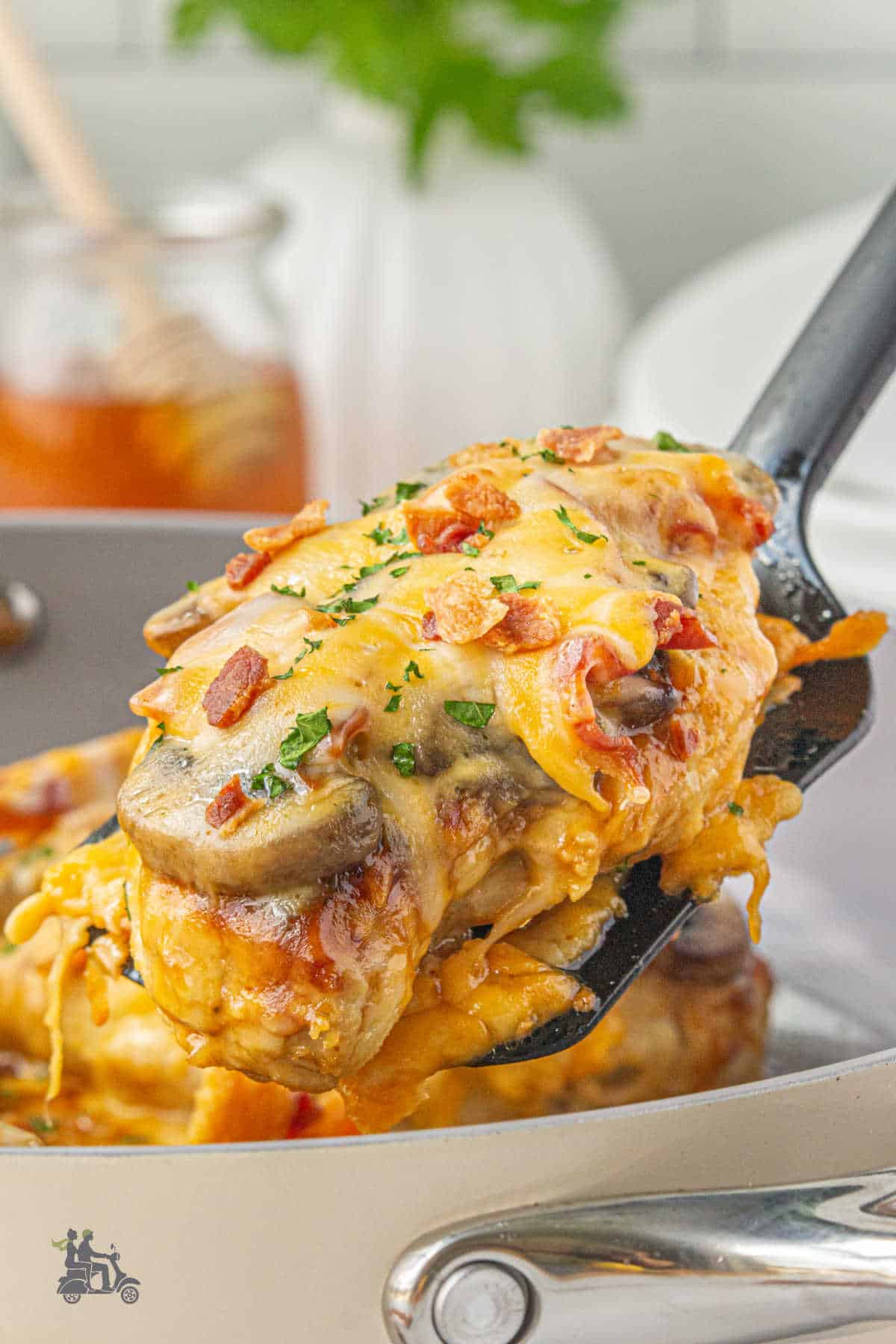A spatula draws up a cooked chicken breast covered with cheese and bathed in a sauce. 