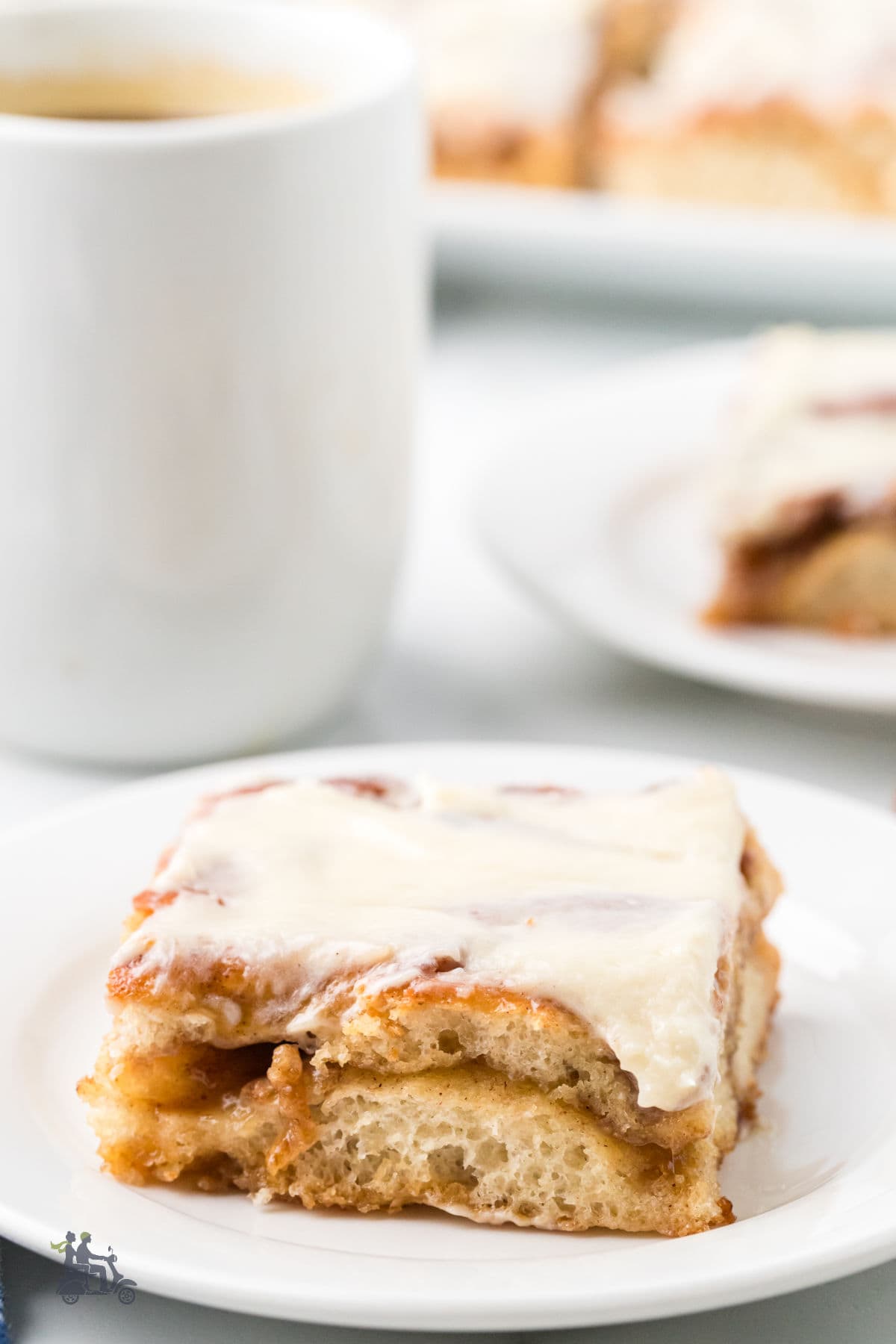Fluffy cinnamon yeast focaccia square with cream cheese glaze on a white plate at the breakfast table. 