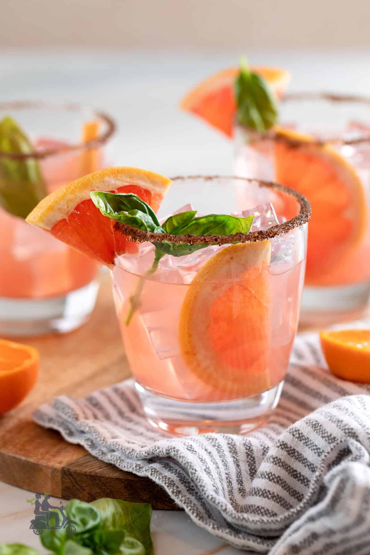 Three glass tumblers filled with grapefruit tangerine, and basil cocktails garnished with grapefruit wedges and basil sprigs.