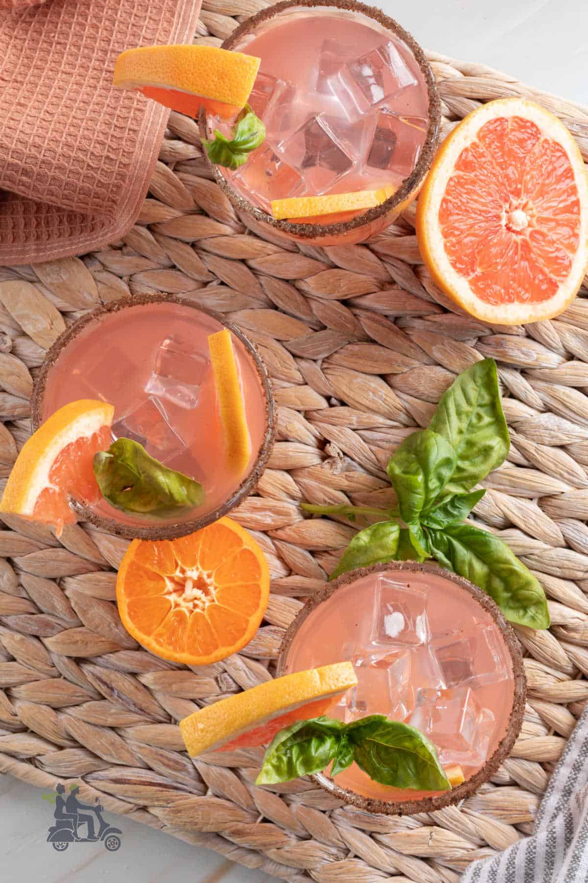 Three tumblers filled with the Grapefruit Basil Gin Cocktail set on a rattan placemat.