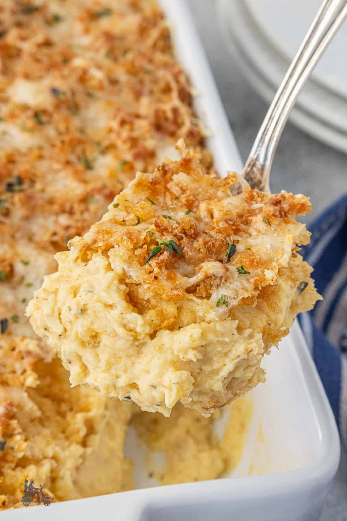 A serving spoon removes of scoop of buttery topped mashed potatoes from the baking dish.