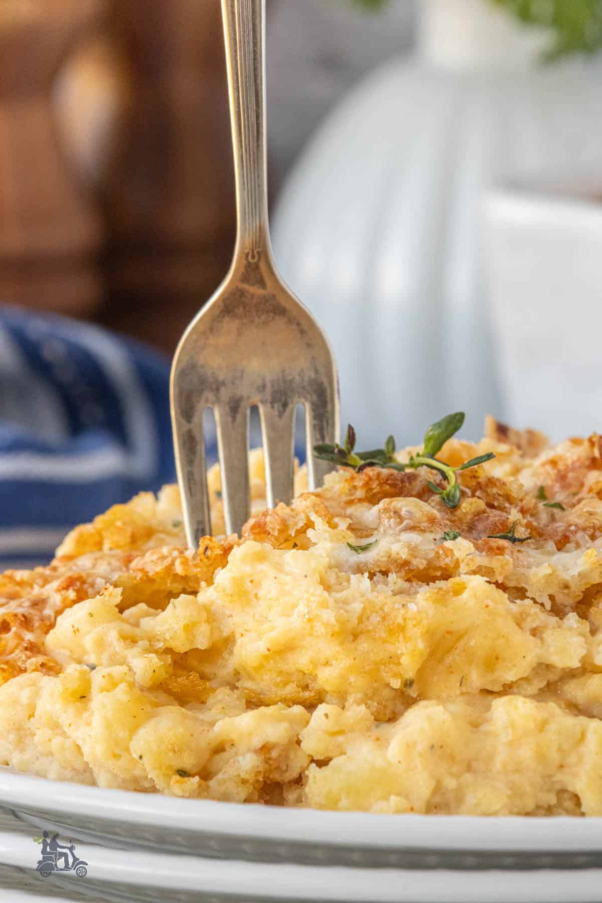 A fork is in the baked mashed potato casserole with Gruyère cheese on a small white plate.