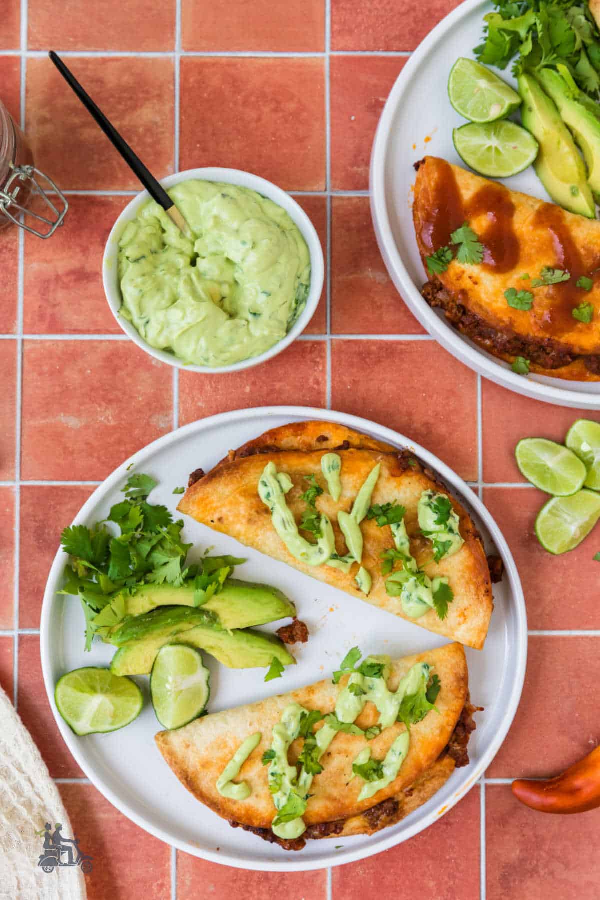 Two of the finished ground beef tacos are on white plate with a bowl of the lime cream sauce on the side.
