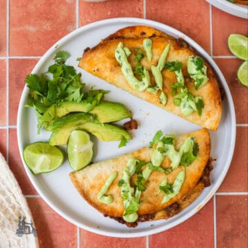 Two oven-baked beef tacos on a white plate with lime wedges, avocado slices, and chopped cilantro.