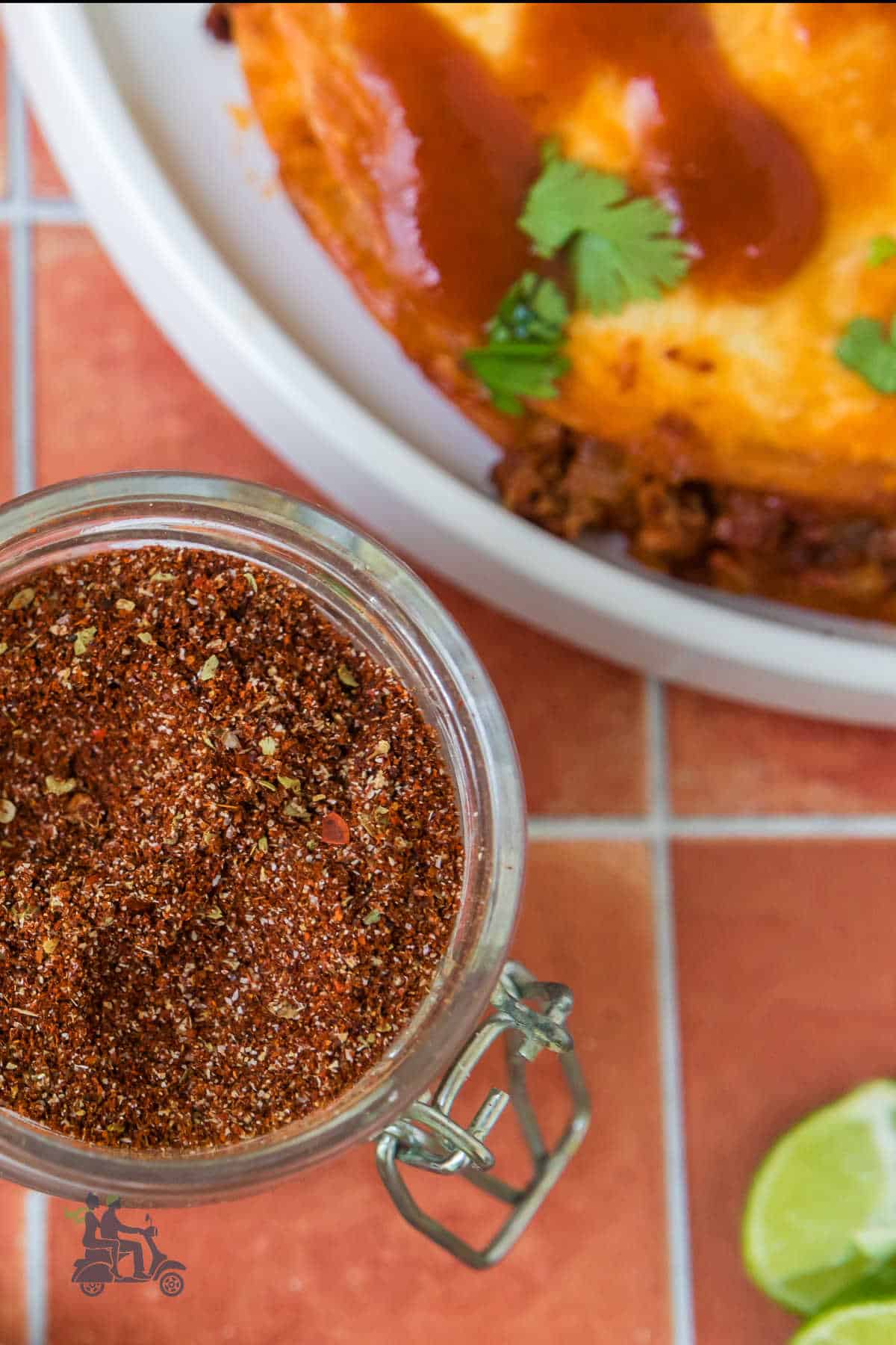 A jar of Taco Seasoning for Beef next to a plate of beef tacos. 