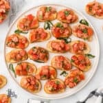 A white platter holds French baguette slices with tomato bruschetta appetizer.
