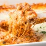 A casserole dish filled with marinara and cheese covered ravioli with a spatula removing a portion.