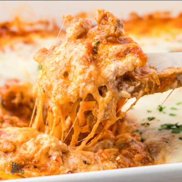 A casserole dish filled with marinara and cheese covered ravioli with a spatula removing a portion.