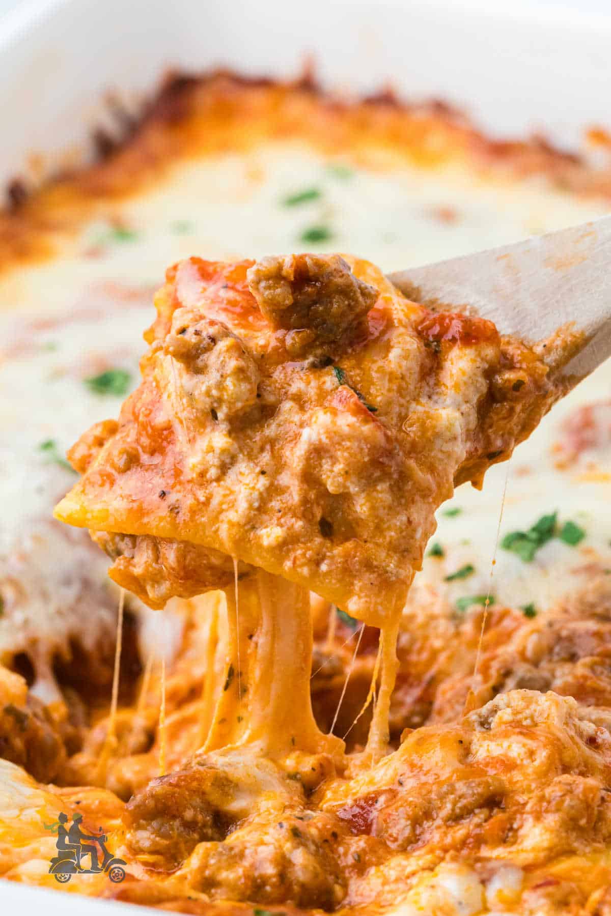 Closeup of a wooden serving spoon scooping up a helping of the baked ravioli recipe.