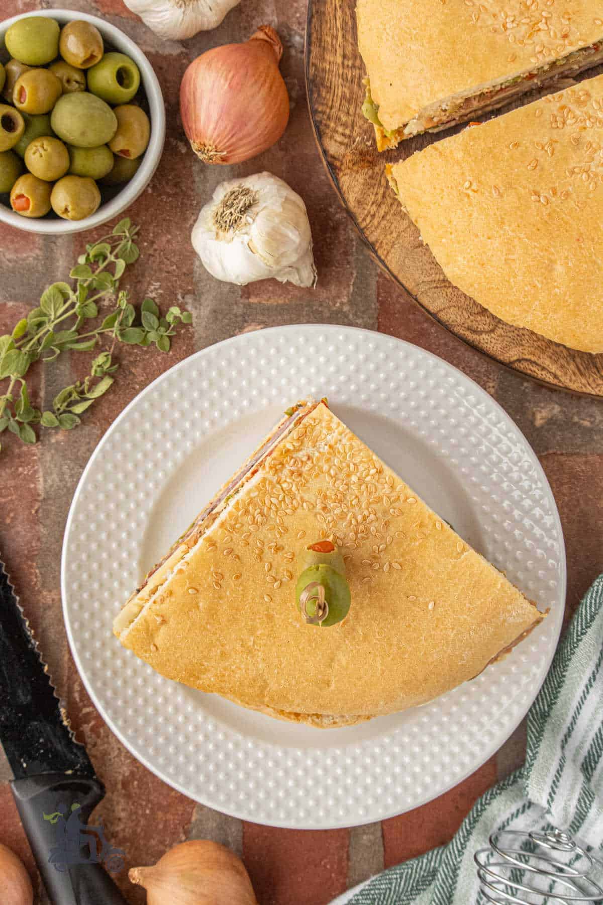 An overhead view of a muffuletta wedge with an olive garnish on a white plate.
