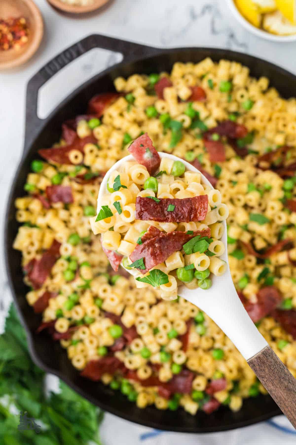 A serving spoon holds up a heaping portion of ditalini and peas garnished with fresh herbs.