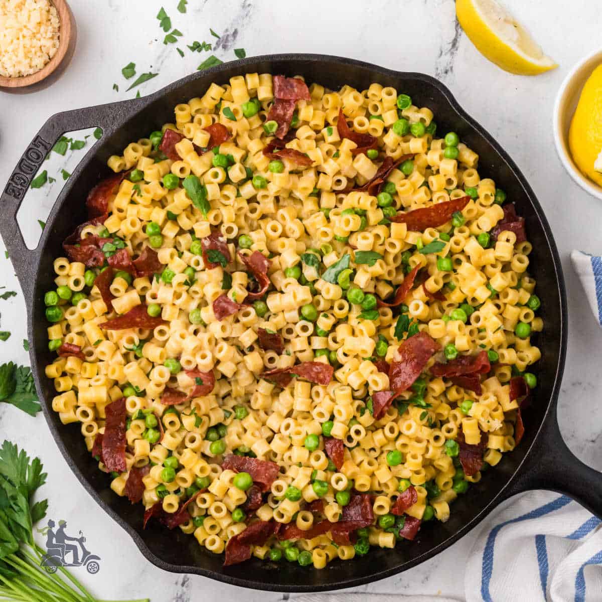 Creamy ditalini pasta with peas in a black cast iron skillet, topped with fresh herbs.