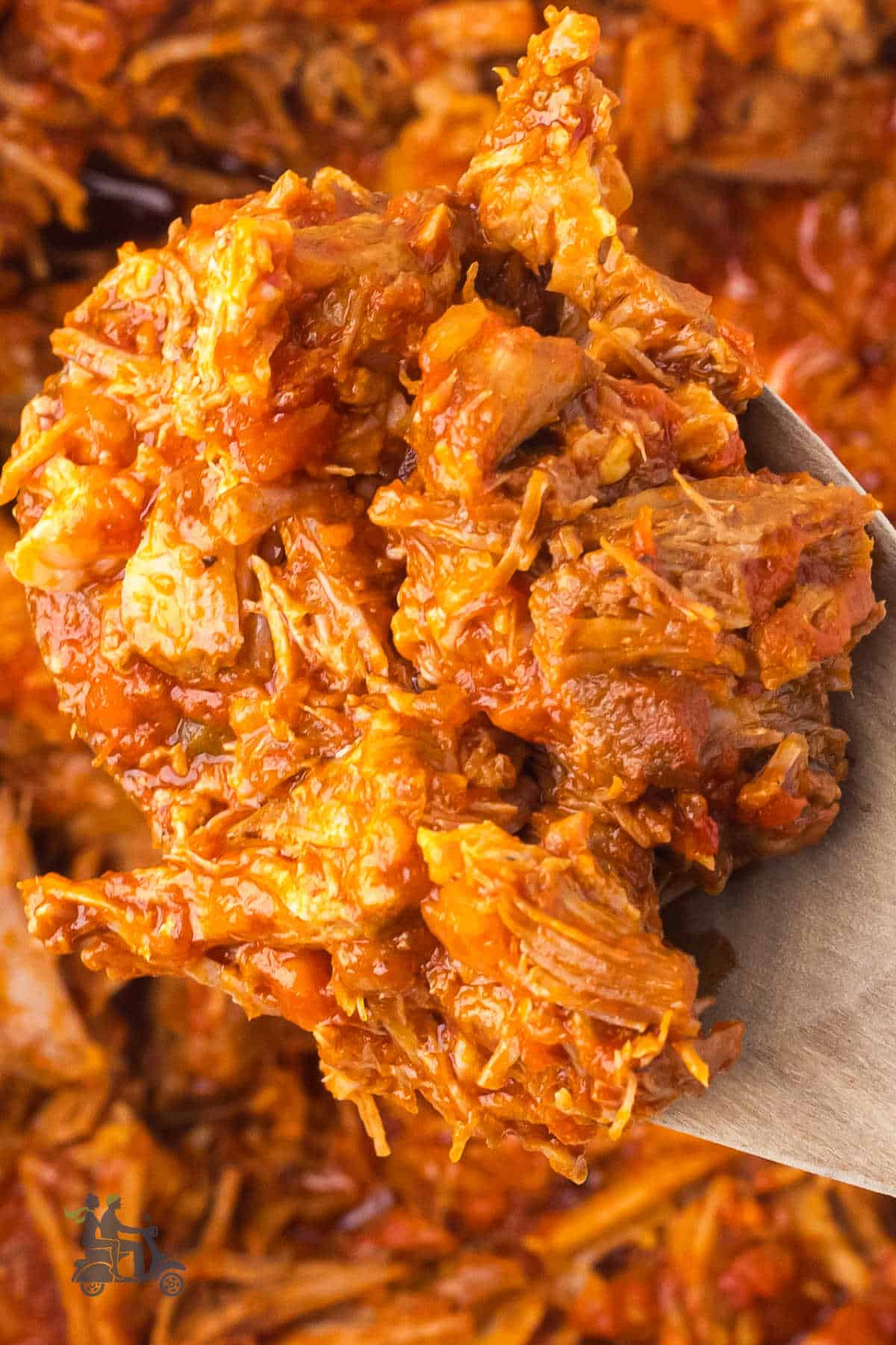 Closeup of a wooden spoon holding a scoop of the shredded pork in the tomato wine sauce.