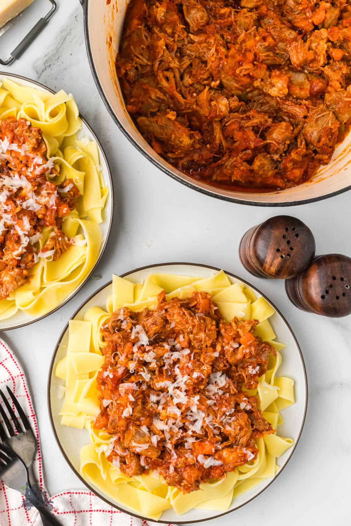 Overhead view of the Pork sauce in a Dutch oven with two plates filled with pappardelle pasta and covered with pork white ragu. 