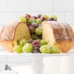 Irish Butter Cake recipe served with frosted Prosecco grapes on a white milk glass cake stand.