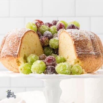 Irish Butter Cake recipe served with frosted Prosecco grapes on a white milk glass cake stand.