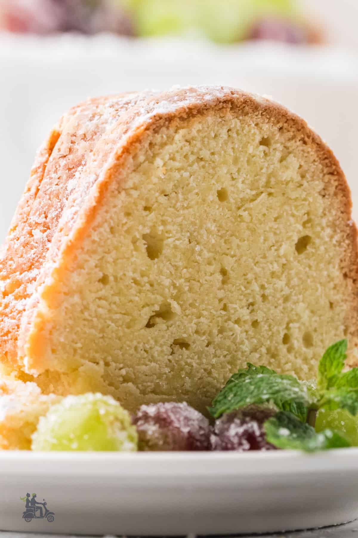 Closeup of the moist Irish Butter cake with powdered sugar served on a white plate with sugar-frosted grapes.