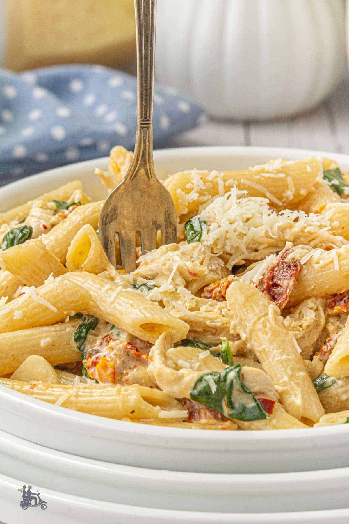 A dinner bowl filled with the penne pasta with oil-packed sun-dried tomatoes and Parmesan cheese.