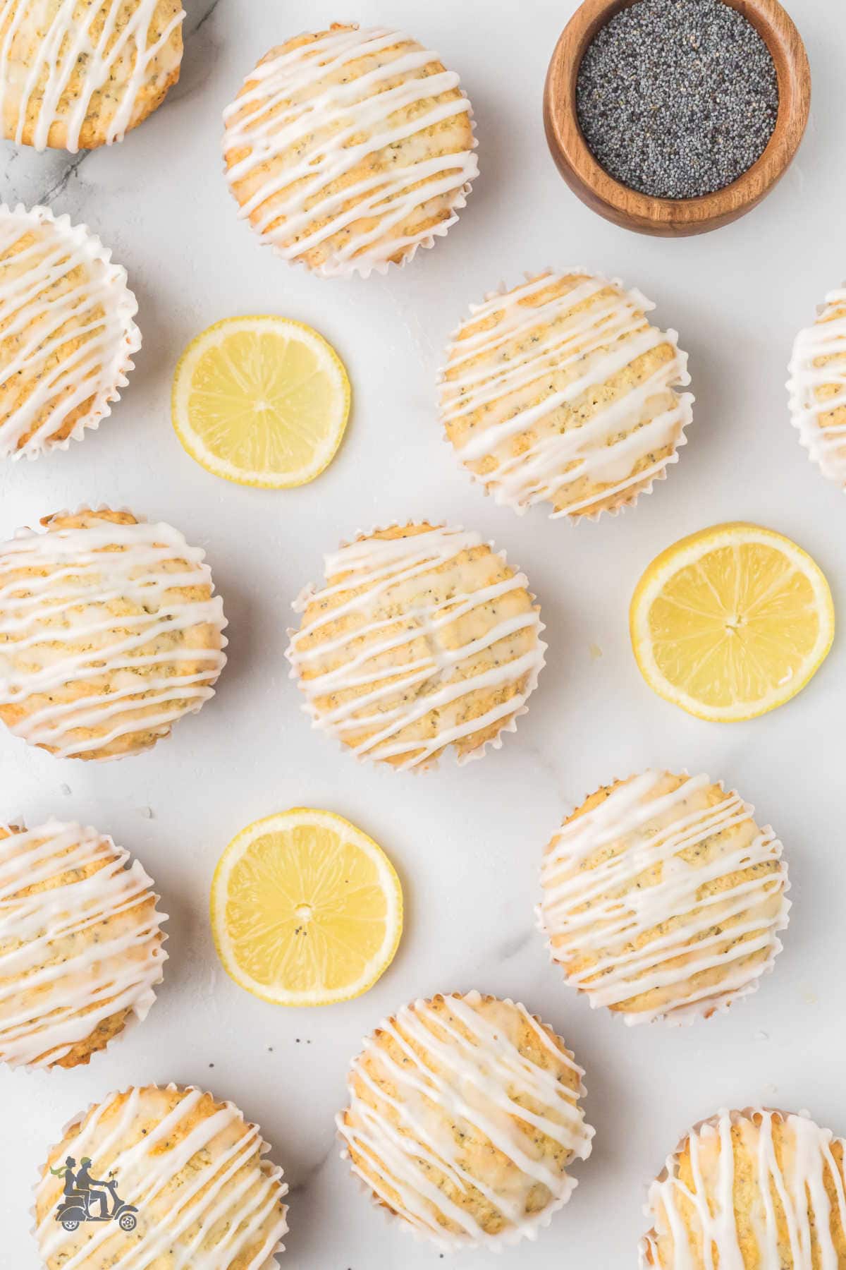 Lemon muffins with poppy seeds and lemon zest are lined up on a white counter.