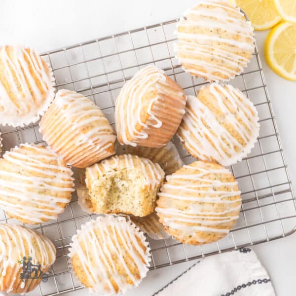 Homemade lemon poppy seed muffins with lemon glaze on a wire cooling rack, with a bite taken from one muffin.