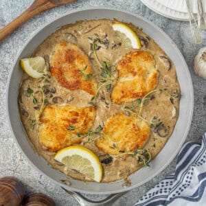 Creamy balsamic chicken and mushroom skillet in a pan with lemon wedges as garnish.