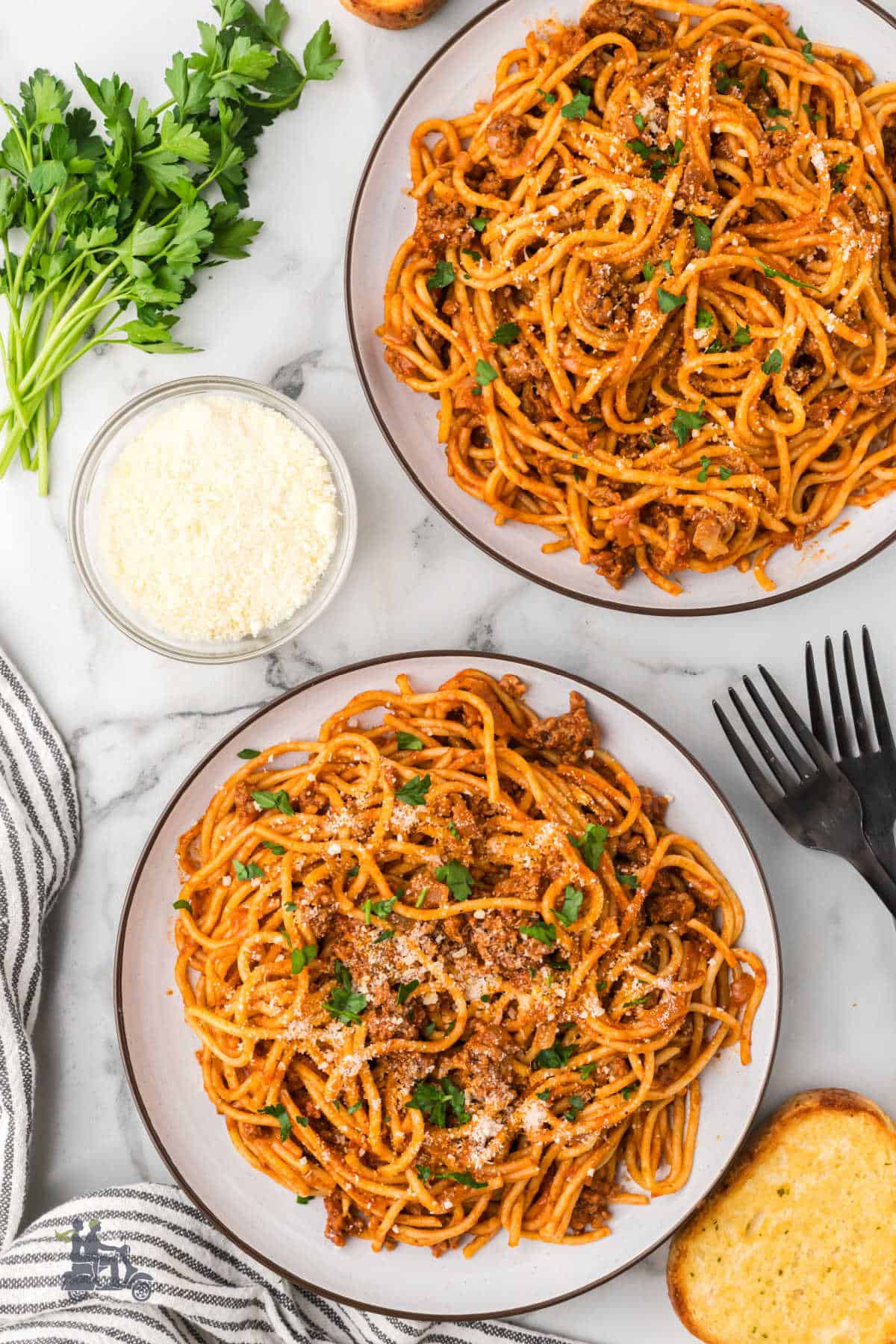 Flavorful one-pot spaghetti with ground beef and spices is plated and garnished with Italian parsley and parmesan cheese.