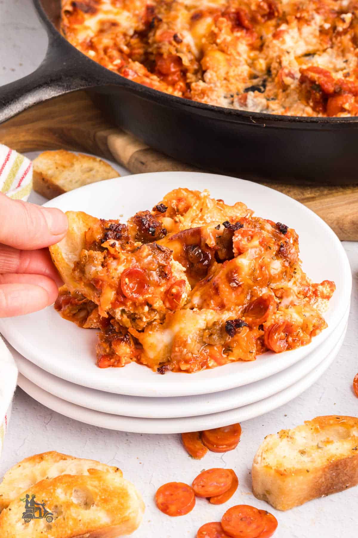 A hand scooping some creamy pizza dip onto a crostini.