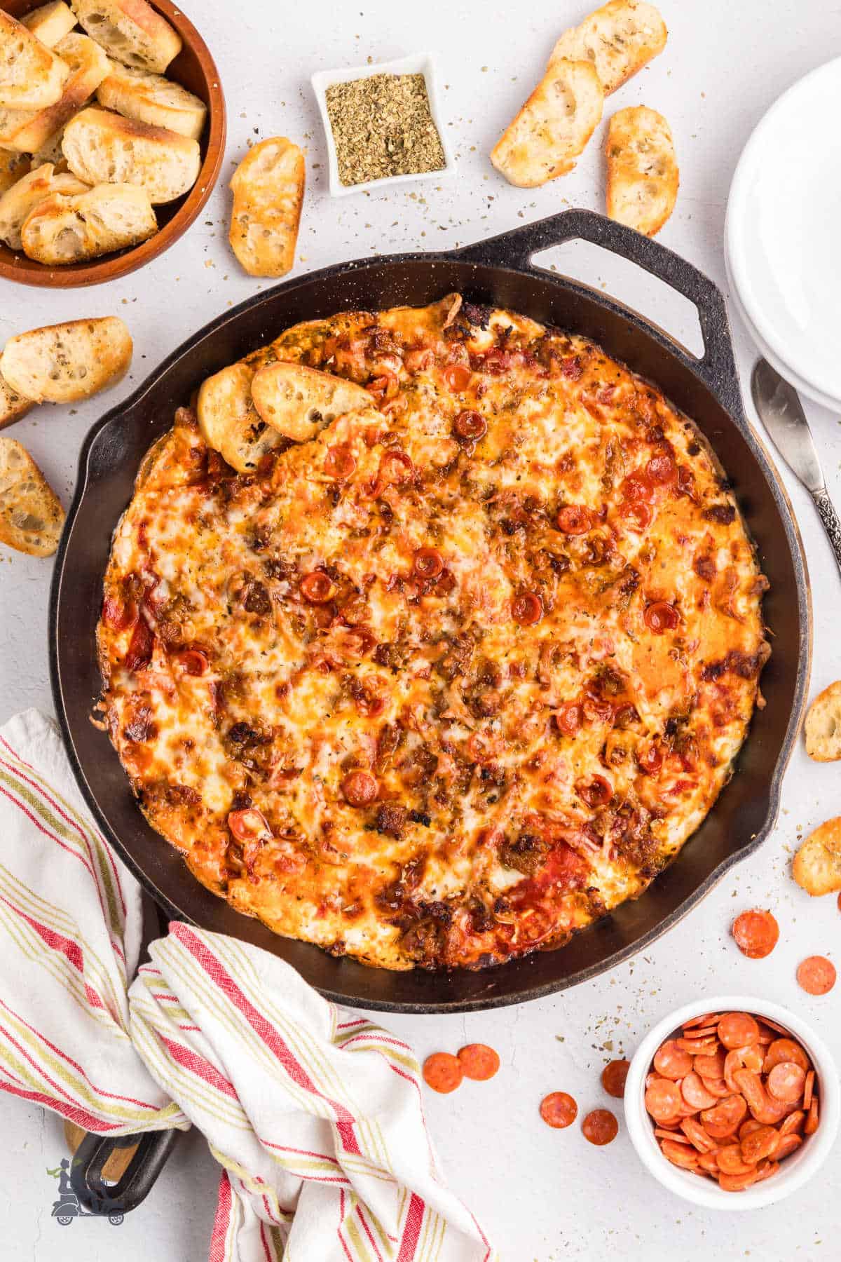 Layered pizza dip appetizer in a black cast iron skillet with Italian bread toast on the side. 