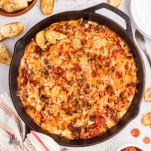 Cast iron skillet filled with cheesy pepperoni pizza dip served with crostini.