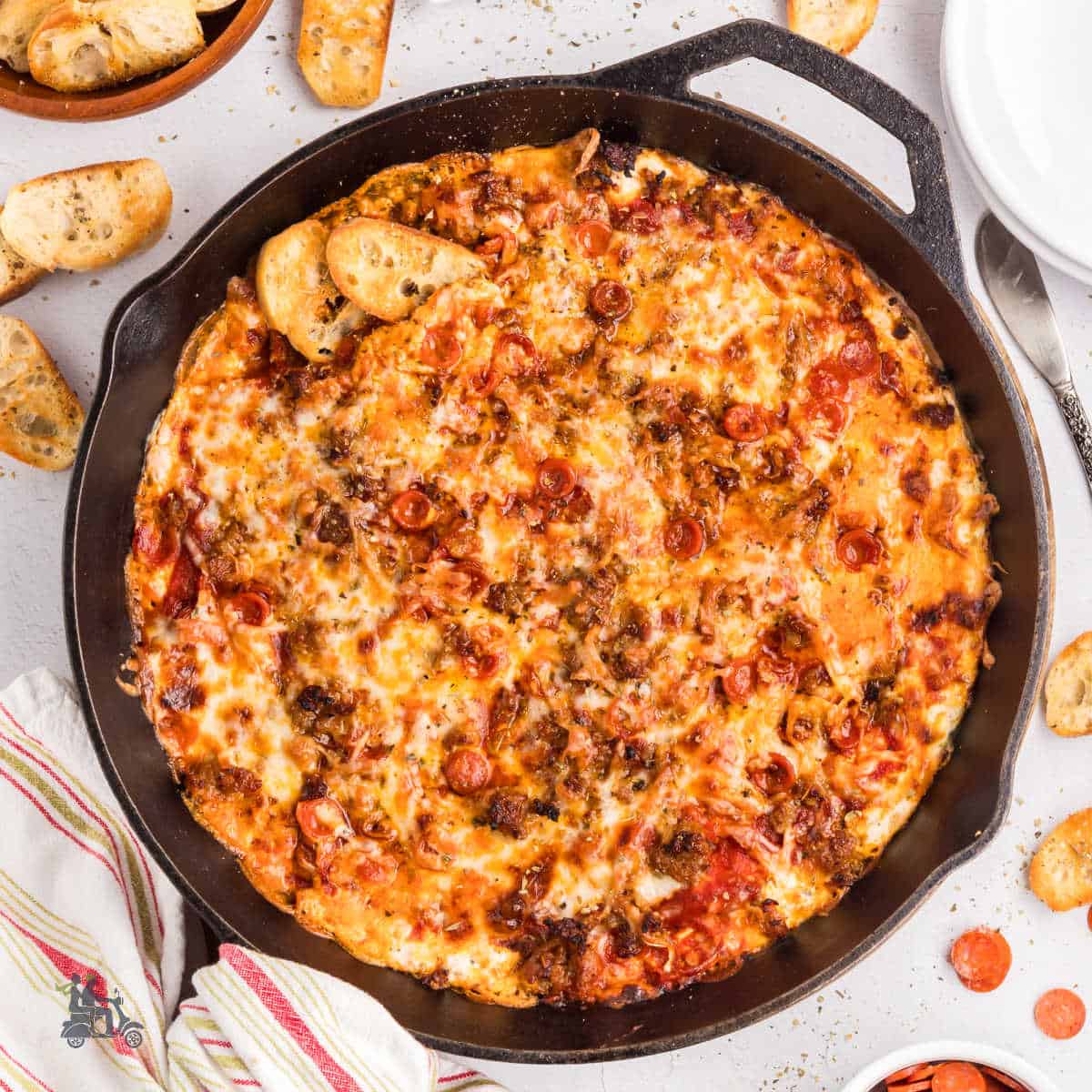 Cast iron skillet filled with cheesy pepperoni pizza dip served with crostini.