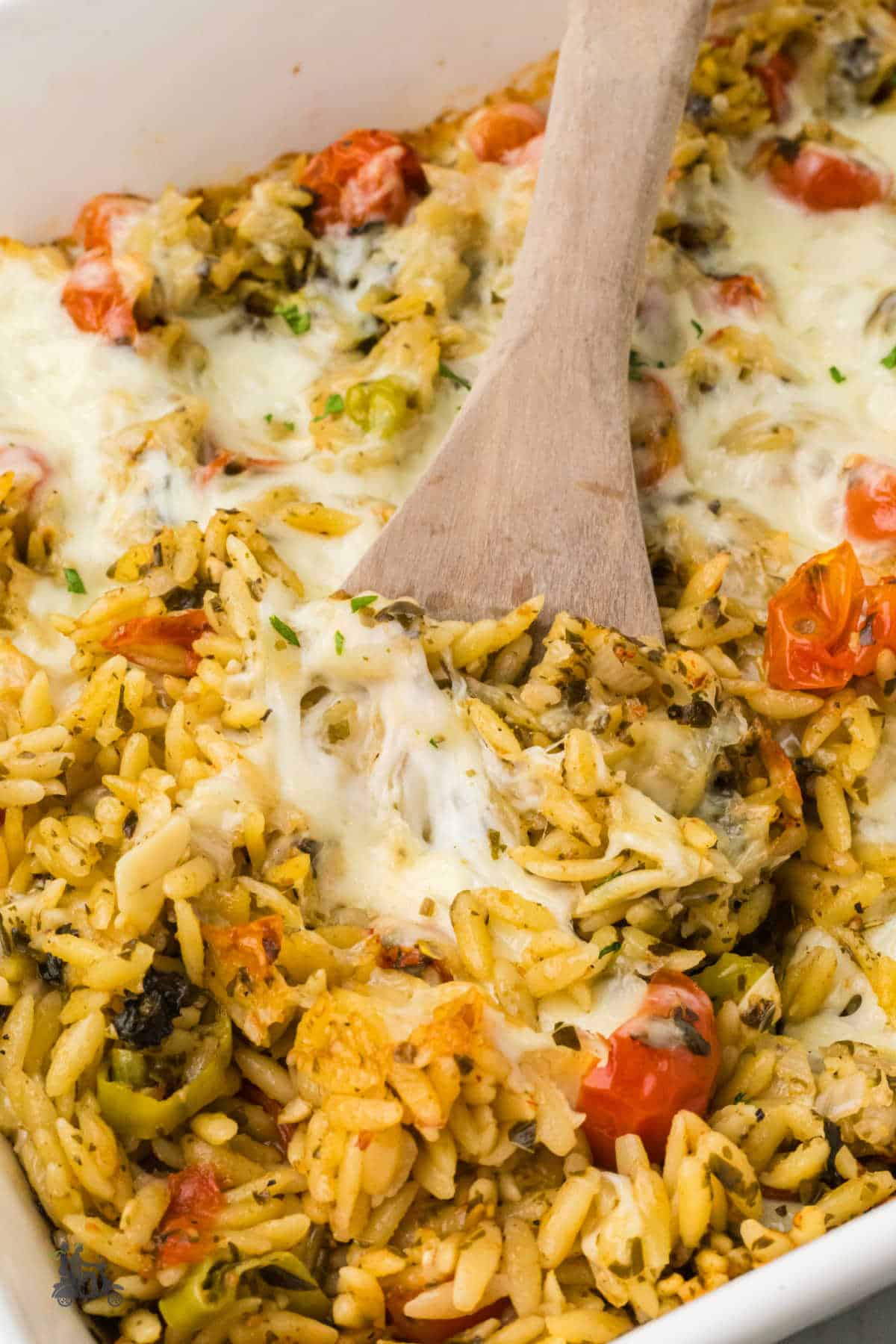Close-up of baked pesto orzo casserole with bubbling mozzarella, cherry tomatoes, and basil fresh from the oven.