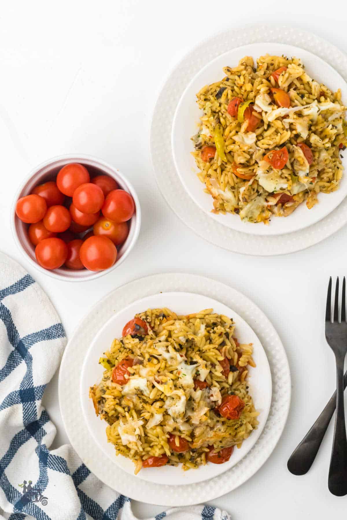 Served portions of Caprese pesto orzo bake with melted mozzarella and roasted cherry tomatoes on dinner plates.