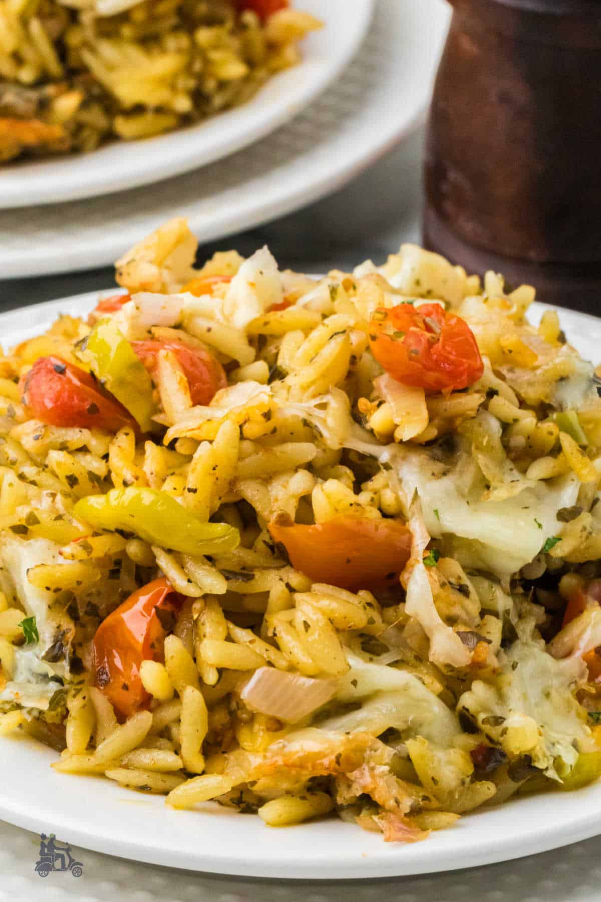 Close-up plated serving of cheesy baked orzo with pesto, tomatoes, and mozzarella cheese.