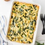 Baked creamed spinach pasta in a casserole dish garnished with chopped Italian parsley.