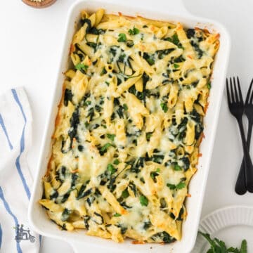 Baked creamed spinach pasta in a casserole dish garnished with chopped Italian parsley.