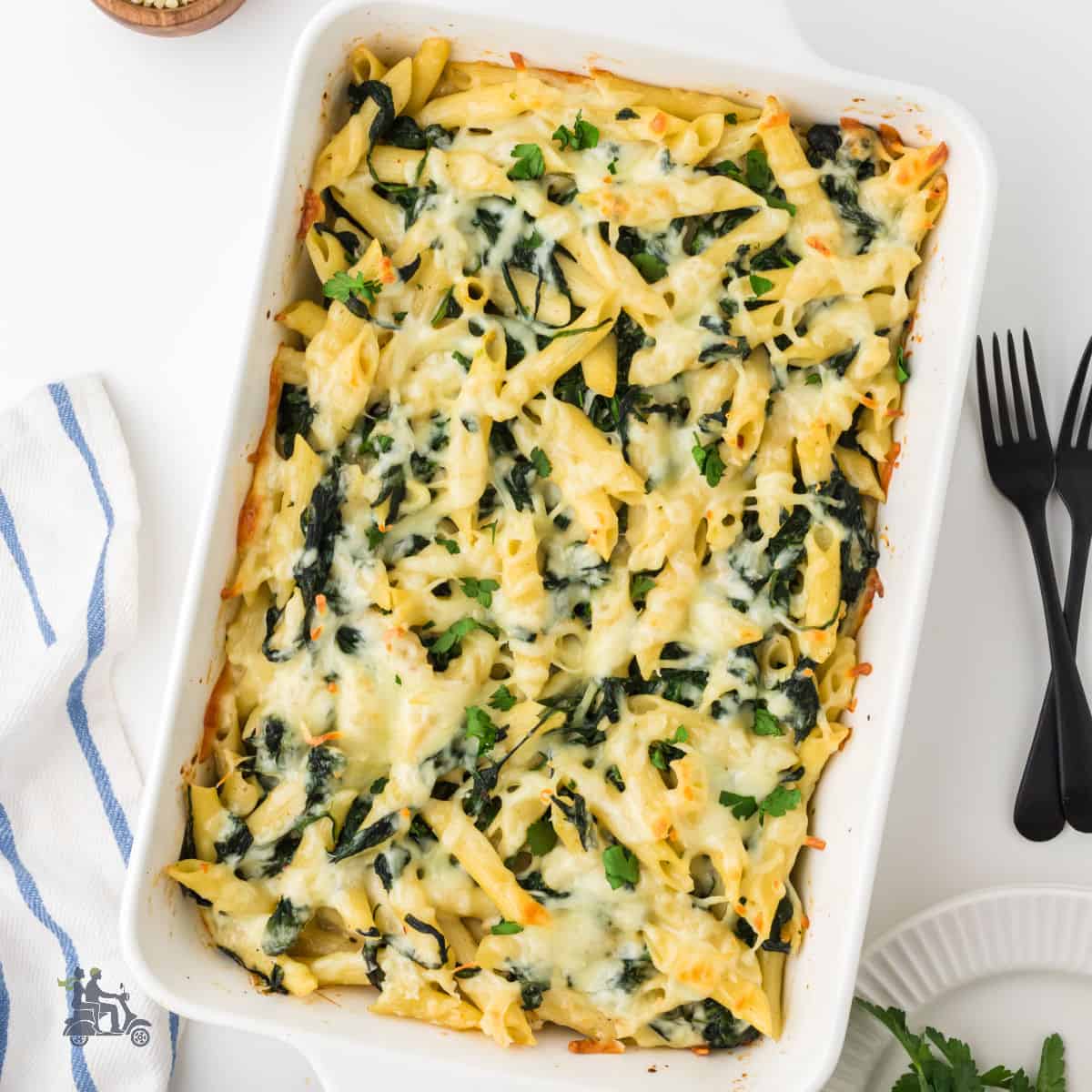Baked creamed spinach pasta in a casserole dish garnished with chopped Italian parsley.