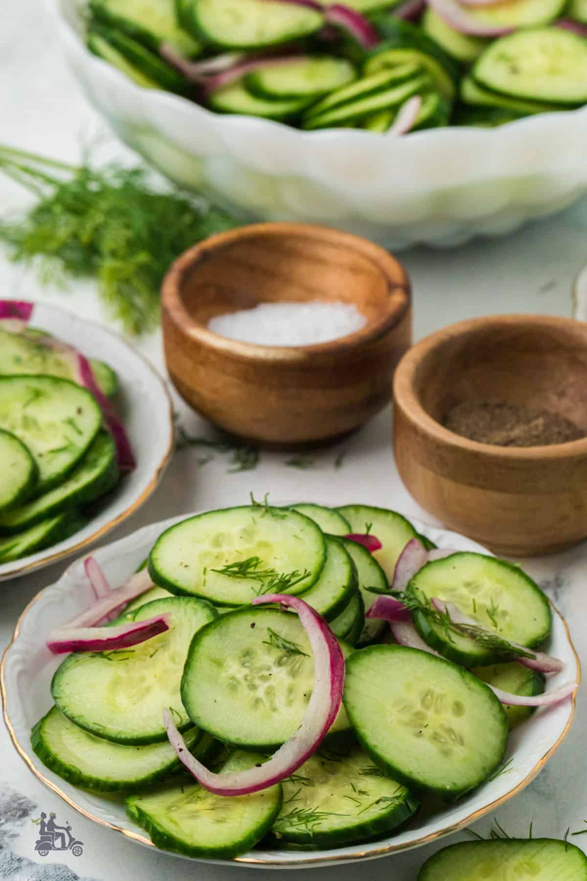 A refreshing summer cucumber and onion salad sits on a white plate. It’s dressed with a bright vinegar dressing, simple and zippy. Salt and pepper are served on the side, so you can season to taste.