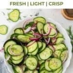 Sliced English cucumbers and red onions tossed in vinegar and dill are shown in a white salad bowl.