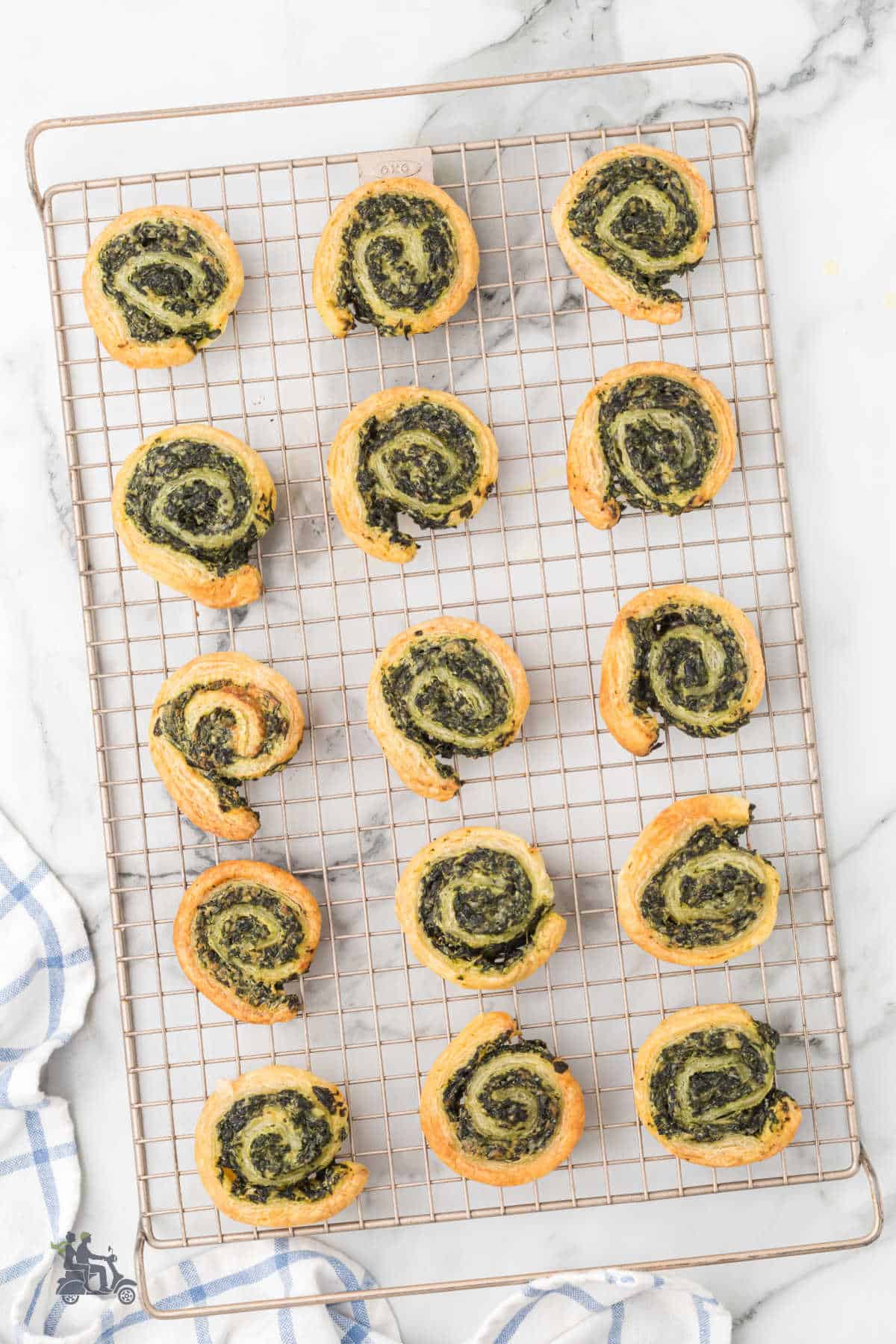 The baked cream cheese and spinach puff pastry pinwheels are cooling on a wire rack.